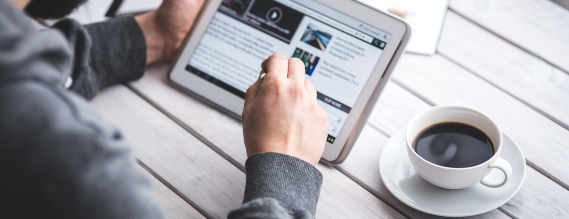 Mand sidder ved bord med en kop kaffe og en iPad